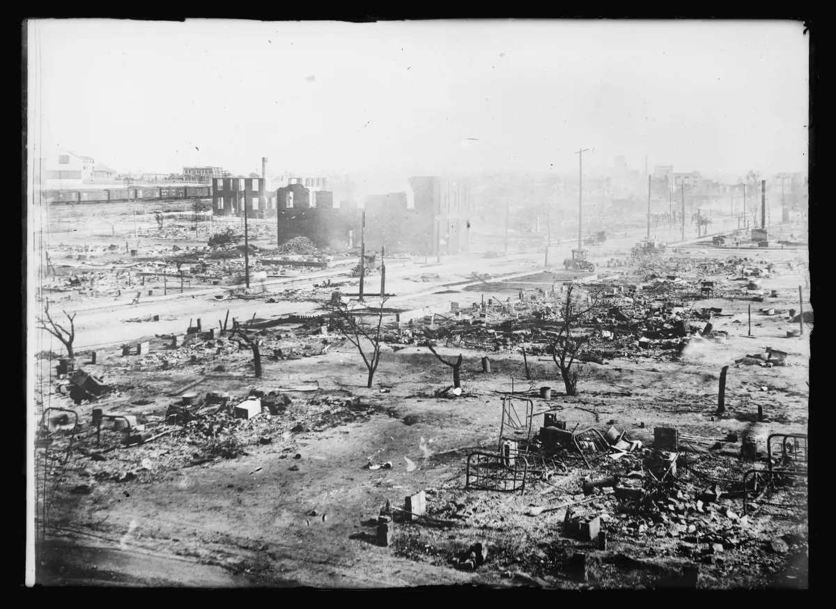 Black-and-white photograph of the Greenwood neighborhood in ruins, June 1921. A wide expanse of cleared ground stretches to the horizon, dotted with chimneys, broken walls, and scorched debris where homes and businesses once stood.