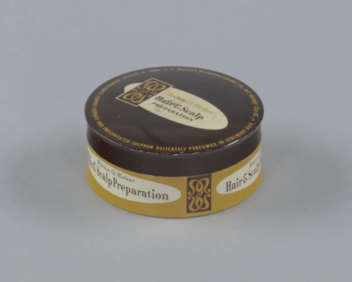 Color photograph of an original metal tin for Madam C.J. Walker's Hair and Scalp Preparation. The tin is rectangular with a hinged lid; product label text and brand mark are visible across the top face.